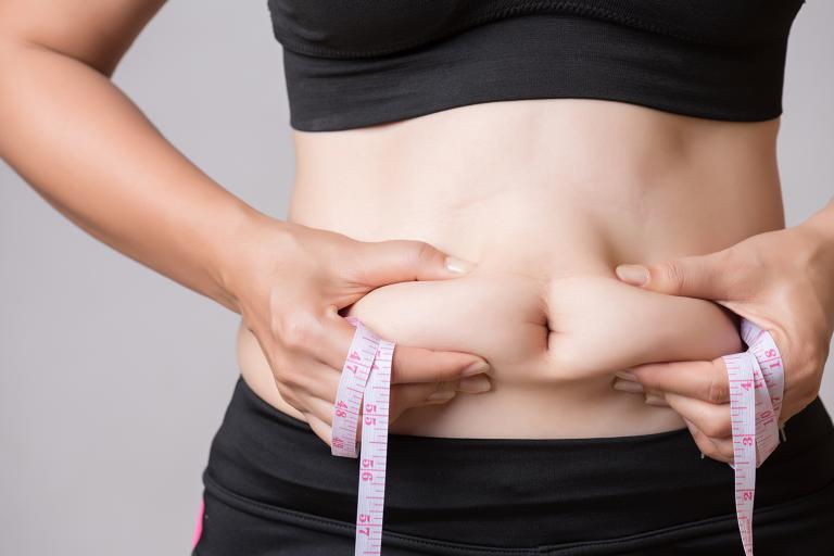 a healthy woman squeezing her excess tummy fat