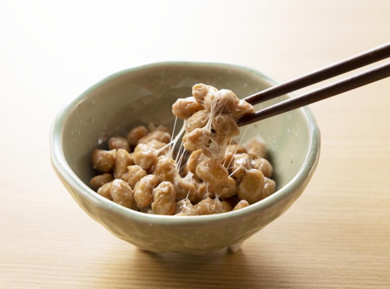 Chopsticks picking up some natto from a small bowl.